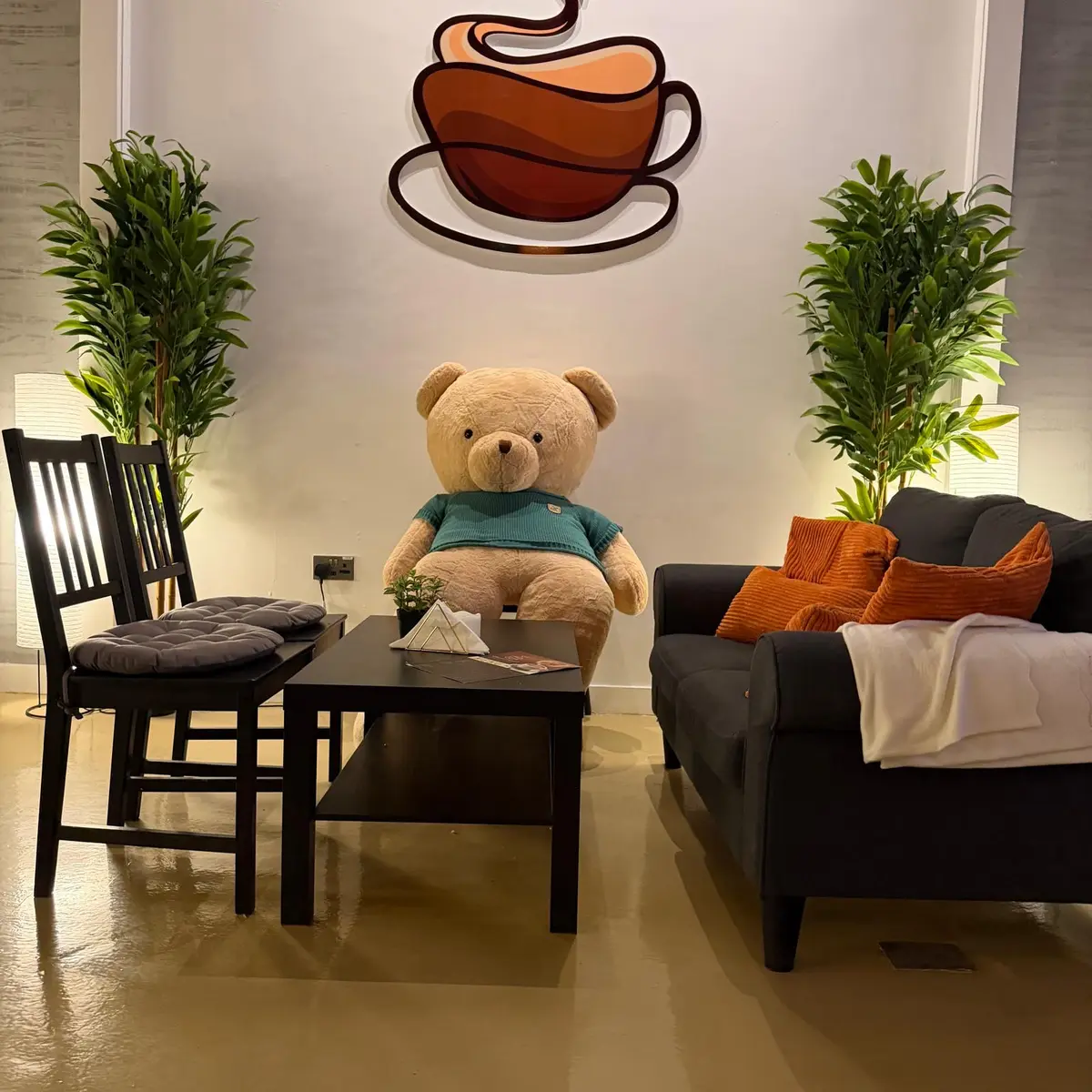 Cozy sofa corner at Espresso Amore with cushions, plants and a teddy bear under the heart-cup logo